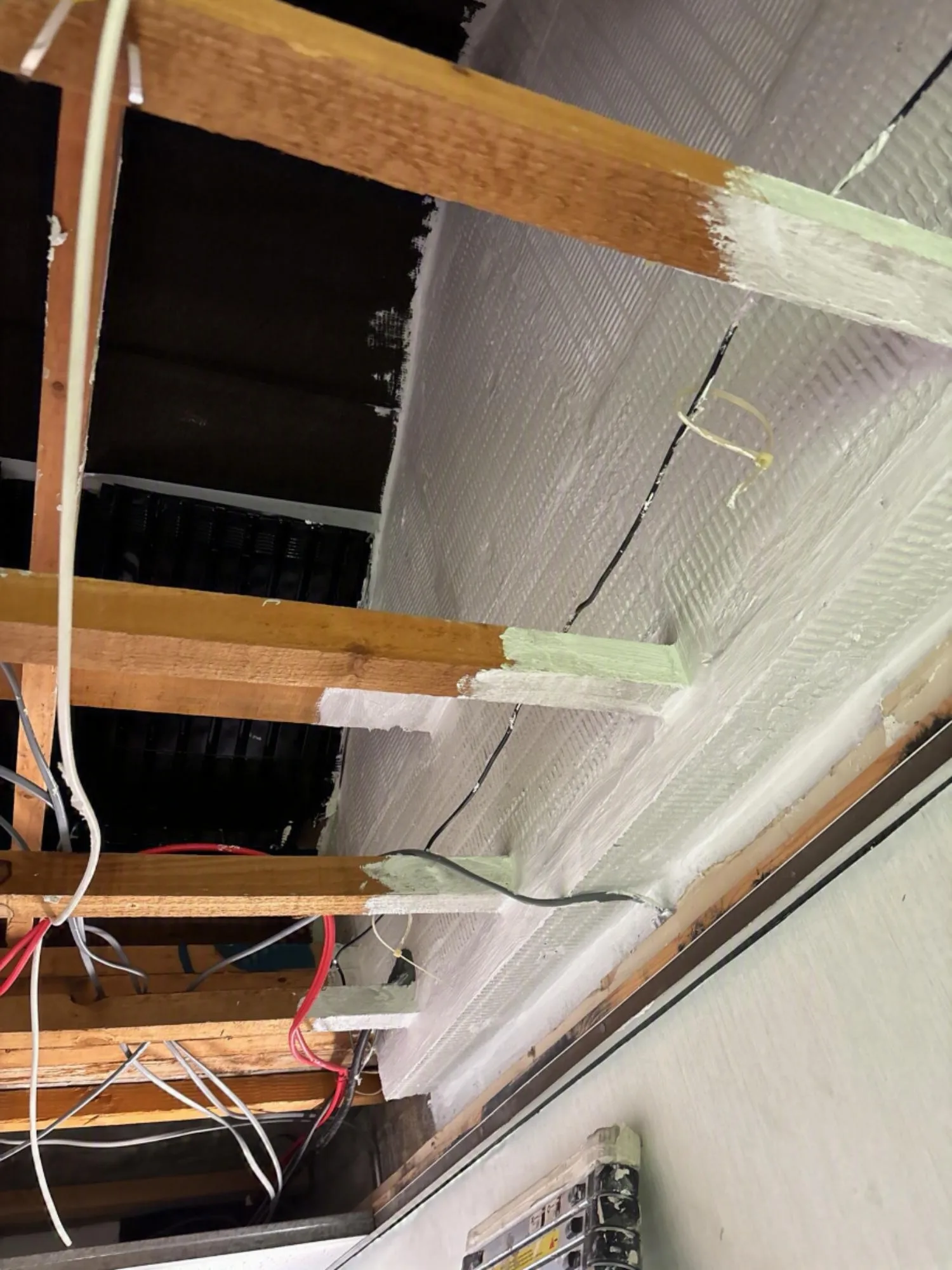 Fire barrier installation showing sealed areas with penetrations and wiring in a loft space