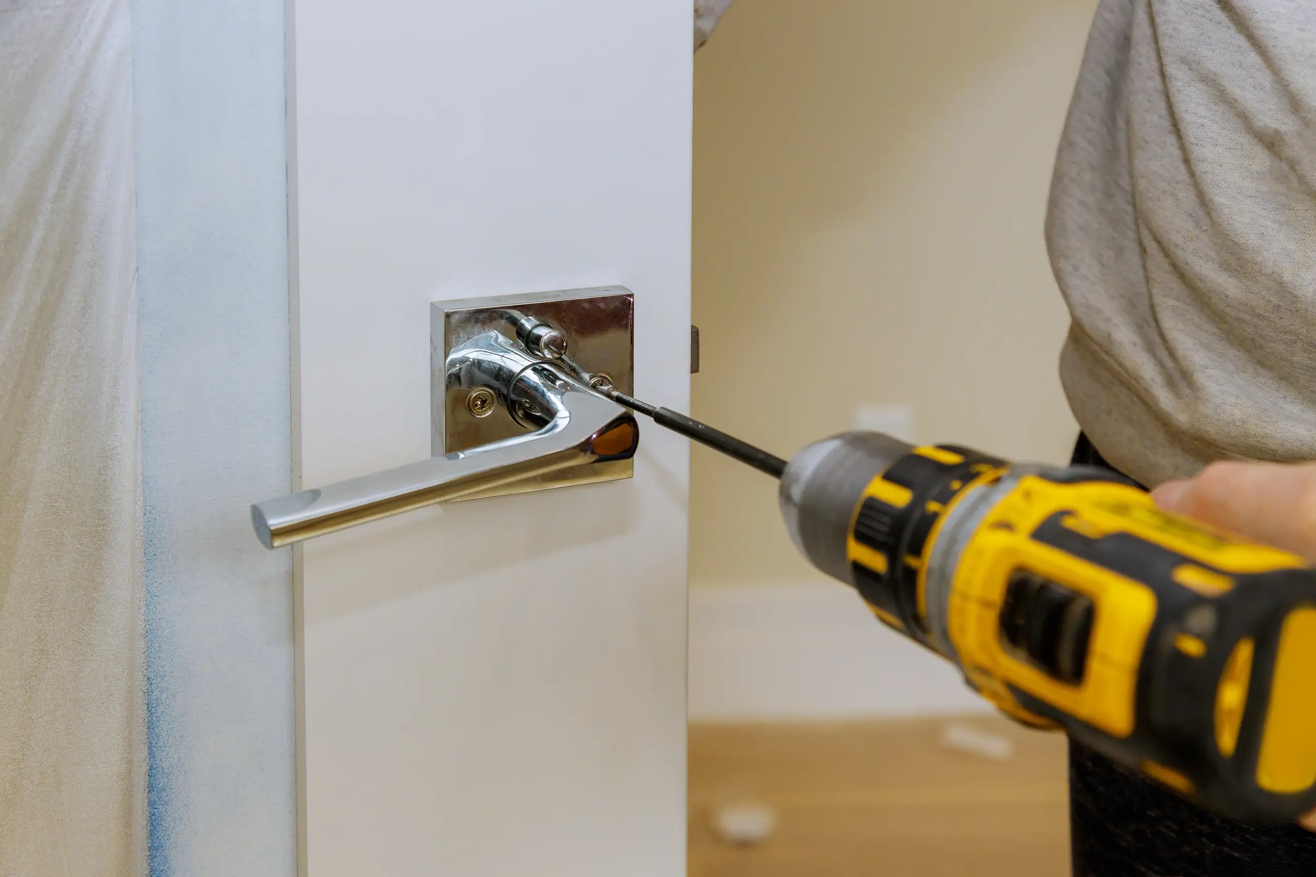 A person using a power drill to install a fire door handle on a white door