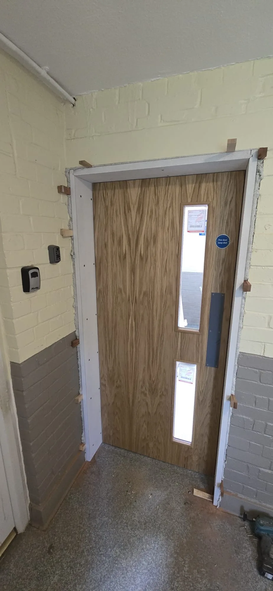 Fire door installation in progress, showcasing a wooden door with windows fitted into the frame